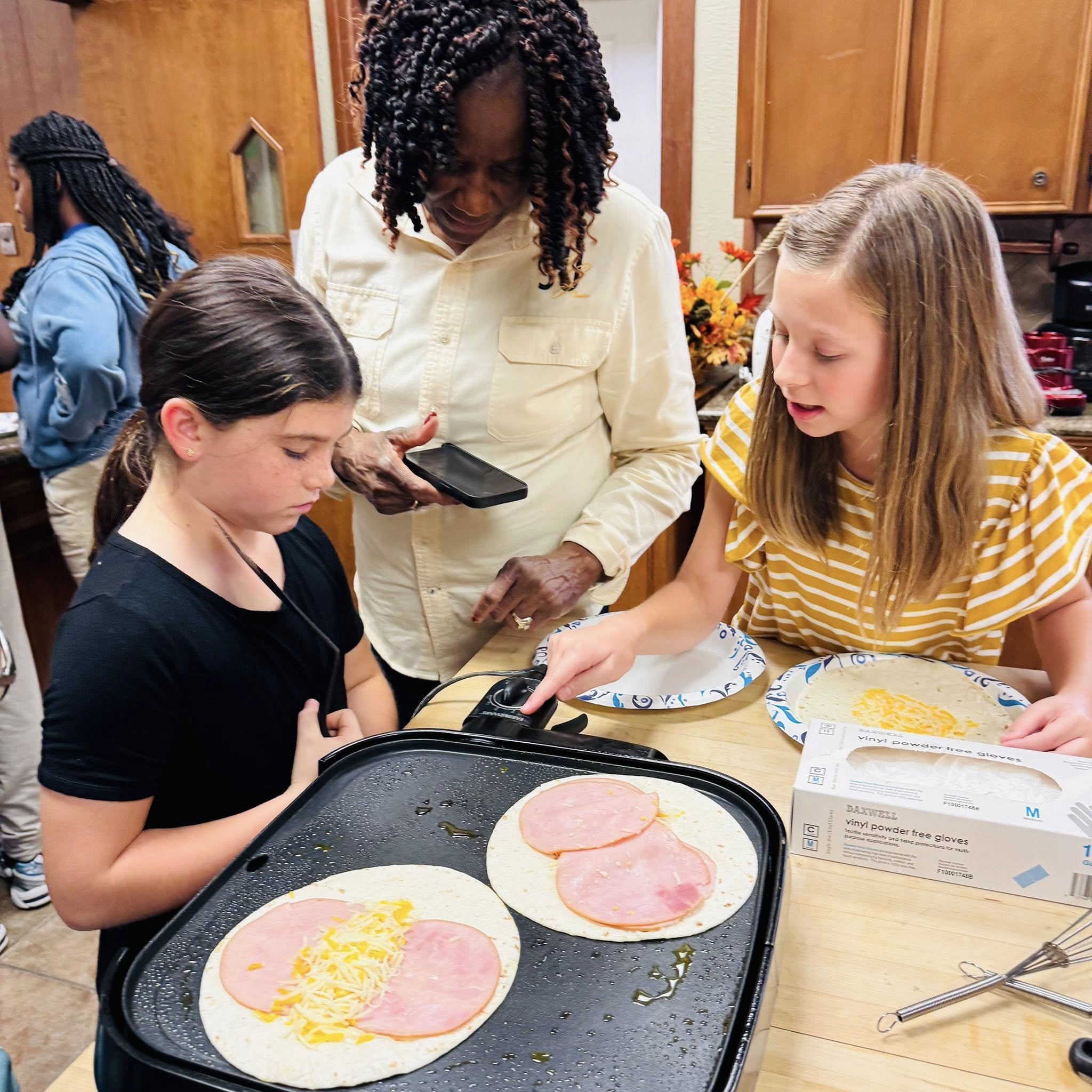 A woman helping two girls cook on a griddle.